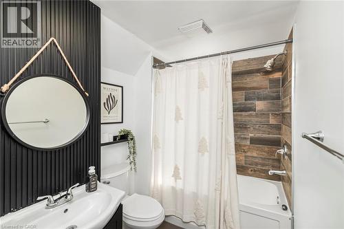 Bathroom featuring a dark vertical slat accent wall, white pedestal sink, and a built-in tub with wood-look tile surround - 114 Weir Street N, Hamilton, ON - Indoor Photo Showing Bathroom