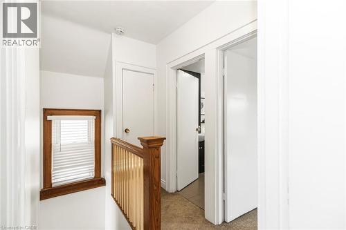 Upper-level hallway featuring a window with wood trim and white blinds, wood-finish stair railing with vertical spindles, and multiple interior doors - 114 Weir Street N, Hamilton, ON - Indoor Photo Showing Other Room