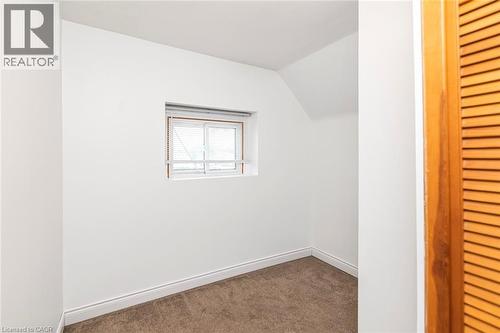 Compact interior space featuring a single window, sloped ceiling, light brown carpet, white baseboards, and a wooden louvered door - 114 Weir Street N, Hamilton, ON - Indoor Photo Showing Other Room