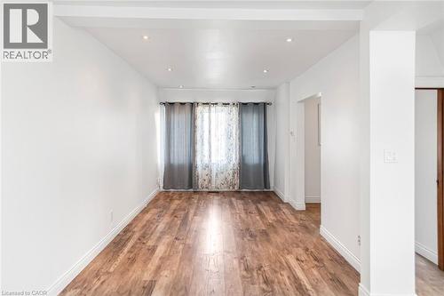 Spacious room featuring wood-finish flooring, white baseboards, and bright white walls - 114 Weir Street N, Hamilton, ON - Indoor Photo Showing Other Room