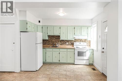 Kitchen featuring mint green cabinetry, a mosaic tile backsplash, a built-in sink, wood-finish countertops, and tile flooring - 114 Weir Street N, Hamilton, ON - Indoor Photo Showing Kitchen