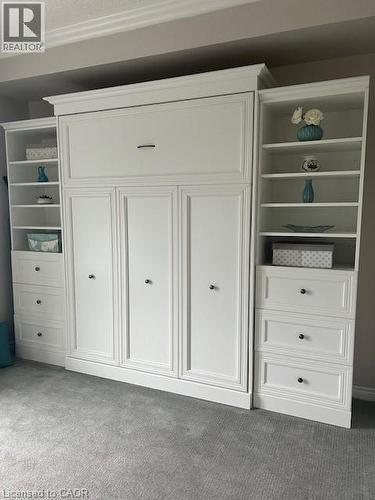 Integrated wall unit featuring a pull-down bed system, flanking open shelving, and built-in drawer storage - 34 Plains Road E Unit# 408, Burlington, ON - Indoor Photo Showing Other Room