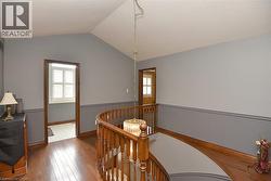Upper-level hallway featuring wood-finish flooring, a curved wooden banister, and a decorative chandelier - 