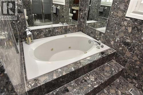 Spa-style jetted tub with polished chrome fixtures, surrounded by extensive stone-finish tiling on walls and a multi-level platform - 36 Tommar Place, Hamilton, ON - Indoor Photo Showing Bathroom