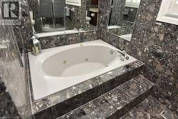Spa-style jetted tub with polished chrome fixtures, surrounded by extensive stone-finish tiling on walls and a multi-level platform - 