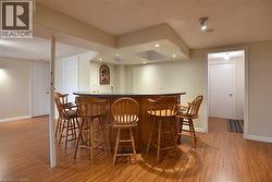 Wood-finish flooring extending throughout a finished lower level, featuring a built-in bar with a dark countertop and recessed lighting - 