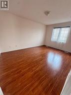 Spacious room featuring wood-finish flooring, light-toned walls, a flush-mount ceiling light fixture, and a window with horizontal blinds and sheer curtains - 