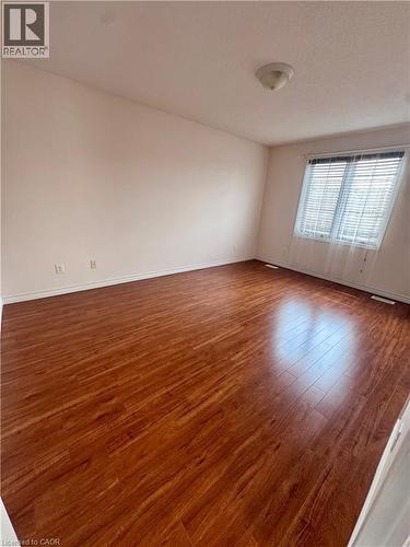 Spacious room featuring wood-finish flooring, light-toned walls, a flush-mount ceiling light fixture, and a window with horizontal blinds and sheer curtains - 452 Beaumont Crescent, Kitchener, ON - Indoor Photo Showing Other Room