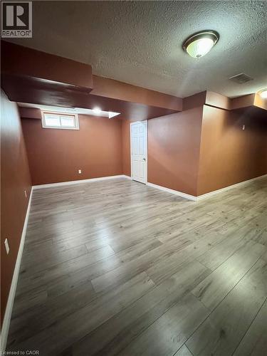 Spacious room featuring wood-finish flooring, warm-toned walls, a white paneled door, and a horizontal window - 452 Beaumont Crescent, Kitchener, ON - Indoor