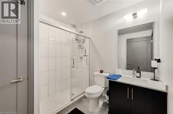 Modern bathroom featuring a glass-enclosed shower with white subway tile, a dark wood-finish vanity with a light-colored countertop, and a large mirror with overhead lighting - 