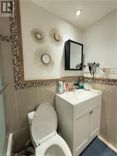Bathroom featuring a white vanity with integrated sink, a wall-mounted storage cabinet with mirrored door, and tiled walls with a decorative mosaic border - 181 Thaler Avenue, Kitchener, ON 