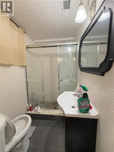 Bathroom featuring a tiled shower enclosure with sliding glass doors, a wall-mounted sink with dark cabinetry, and white subway tile walls - 181 Thaler Avenue, Kitchener, ON 