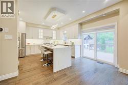 Contemporary kitchen featuring wood-finish flooring, white cabinetry, a large center island with a waterfall countertop, recessed lighting, and stainless steel appliances - 