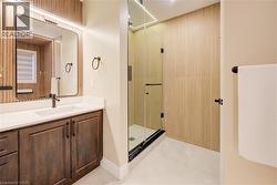 Bathroom featuring a glass-enclosed shower, a vanity with a white countertop and wood-finish cabinetry, and light wood paneling - 