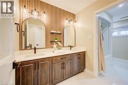 Double vanity featuring dark wood-finish cabinetry, white countertops, and arched mirrors - 
