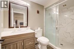 Contemporary bathroom featuring a wood-finish vanity with a white countertop and undermount sink, a framed mirror, and a glass-enclosed shower with white veined wall tiling - 