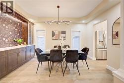 Dining area featuring an elongated chandelier, tray ceiling, and light wood-finish flooring - 