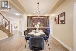 Dining area featuring a contemporary linear chandelier, tray ceiling, and built-in cabinetry with glass panel doors - 