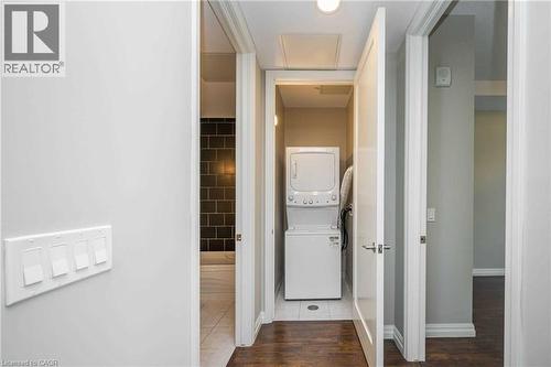 Dedicated laundry closet featuring a stacked washer and dryer, adjacent to a bathroom with dark rectangular wall tiles and a white bathtub - 112 King Street E Unit# 907, Hamilton, ON 