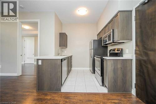 Modern kitchen featuring wood-finish cabinetry, stainless steel appliances, a white countertop, and white floor tiling - 112 King Street E Unit# 907, Hamilton, ON 