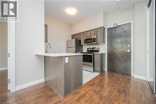 Kitchen area featuring contemporary cabinetry, stainless steel appliances, a breakfast bar with a white countertop, and wood-finish flooring - 112 King Street E Unit# 907, Hamilton, ON 