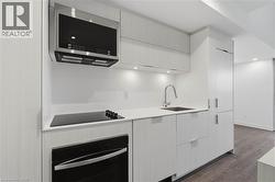 Contemporary kitchen featuring integrated appliances, white flat-panel cabinetry, a stainless steel microwave, a built-in oven, and a ceramic cooktop - 