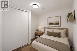 Bedroom featuring wood-finish flooring, white walls, and a ceiling-mounted light fixture - 