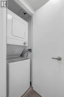 Dedicated laundry closet featuring a stacked white washer and dryer, finished with wood-look flooring and a contemporary brushed nickel door handle - 