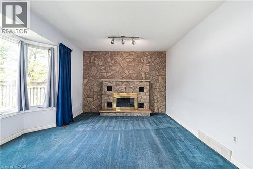 Spacious room featuring a stone-clad fireplace with a brass-trimmed insert, blue carpeting, and a bay window - 381 Kerman Avenue, Grimsby, ON - Indoor With Fireplace