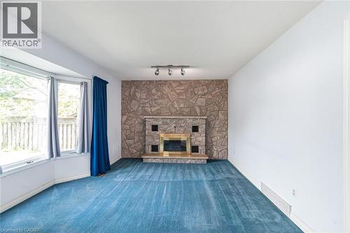 Living area featuring a stone accent wall with an integrated fireplace and brass trim - 381 Kerman Avenue, Grimsby, ON - Indoor Photo Showing Living Room With Fireplace