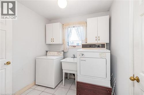 Laundry room featuring a utility sink, white wall-mounted cabinetry, white tile flooring, and a window for natural light - 381 Kerman Avenue, Grimsby, ON - Indoor Photo Showing Laundry Room