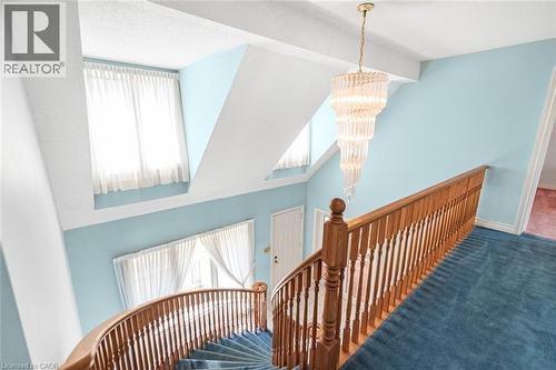 Staircase featuring a wood-finish handrail and balusters, a tiered crystal chandelier, and a curved design - 381 Kerman Avenue, Grimsby, ON - Indoor Photo Showing Other Room