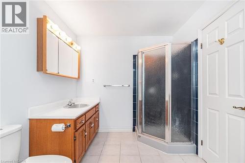 Bathroom featuring a wood-finish vanity with a white countertop and integrated sink, a mirrored medicine cabinet with strip lighting, a corner shower with glass enclosure and dark tile surround, and l - 381 Kerman Avenue, Grimsby, ON - Indoor Photo Showing Bathroom