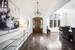 Grand entryway featuring a solid wood door with arched transom, a large arched window, vaulted ceilings, a chandelier, and wood-finish flooring - 