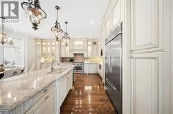 Gourmet kitchen featuring a substantial island with an undermount sink, stone countertops, integrated stainless steel appliances, extensive cream-toned cabinetry, and wood-finish flooring - 