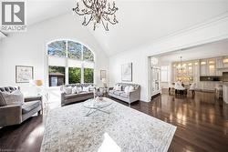 Living area featuring high vaulted ceilings, an arched window, dark wood-finish flooring, and an ornate chandelier - 