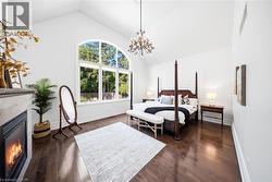 Vaulted ceiling with an elegant chandelier, wood-finish flooring, and a fireplace with a decorative mantel - 