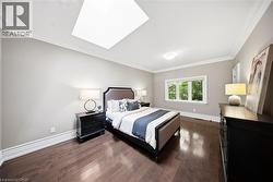 Spacious bedroom with rich wood-finish flooring and extensive crown molding - 