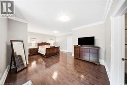 Spacious interior room featuring rich wood-finish flooring, light neutral-toned walls, and elegant crown molding - 