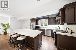 Spacious kitchen featuring an expansive center island with seating, rich wood cabinetry, stainless steel appliances, and wood-finish flooring - 