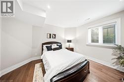 Bright bedroom featuring wood-finish flooring, white baseboards, and a window with horizontal blinds - 