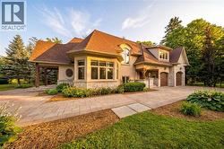 Stately residence featuring a multi-gabled roof, stone and stucco exterior, arched garage doors, an expansive paver driveway, and a covered entry with timber columns - 