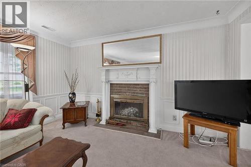 Formal living area featuring a brick fireplace with a white mantel, textured wallpaper, crown molding, and wainscoting - 114 E Second Road E, Stoney Creek, ON 