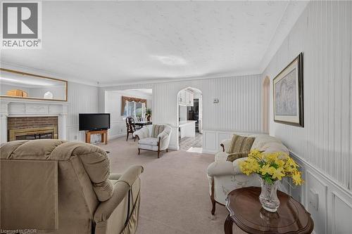 Living area featuring a brick fireplace with a white mantel, textured white wallpaper, light-colored carpeting, and crown molding - 114 E Second Road E, Stoney Creek, ON 