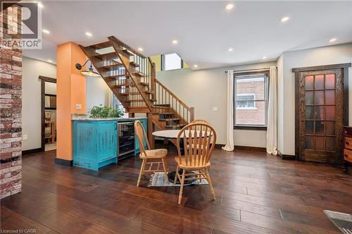 Hardwood flooring throughout, featuring a natural wood staircase with black metal balusters, exposed brick accent wall, and a built-in turquoise cabinet with a beverage cooler and stone countertop - 838 Moore Street, Cambridge, ON - Indoor Photo Showing Other Room