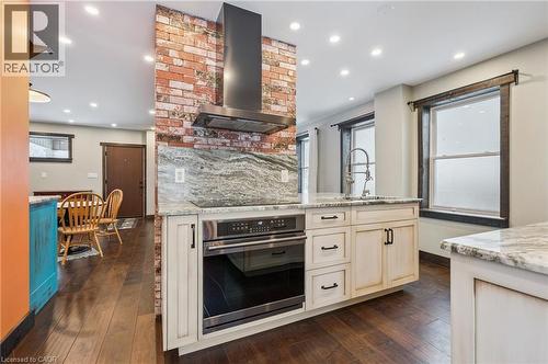 Kitchen featuring an exposed brick accent wall, built-in stainless steel oven, white cabinetry, integrated sink with gooseneck faucet, and stone countertops - 838 Moore Street, Cambridge, ON - Indoor Photo Showing Kitchen