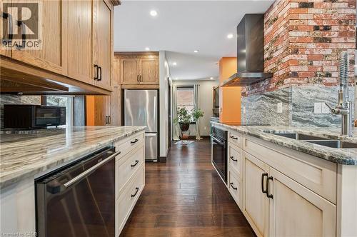 Kitchen featuring wood-finish flooring, light-toned cabinetry, stainless steel appliances, and a brick accent wall with a range hood - 838 Moore Street, Cambridge, ON - Indoor Photo Showing Kitchen With Double Sink With Upgraded Kitchen