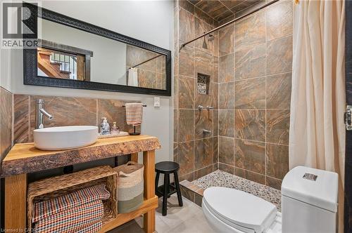Bathroom featuring a live-edge wood vanity with a vessel sink, a stone tile backsplash, a large framed mirror, and a tiled shower with a pebble floor and recessed niche - 838 Moore Street, Cambridge, ON - Indoor Photo Showing Bathroom