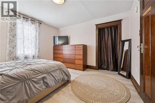 Room featuring light wood-finish flooring, a window with sheer curtains, a recessed closet opening with dark drapery, and a classic wood-paneled door with clear knob hardware - 838 Moore Street, Cambridge, ON - Indoor Photo Showing Bedroom