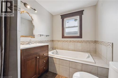 Bathroom featuring a built-in tub with surrounding tile, a window with dark wood trim, a wood-finish vanity with an integrated sink, and an ornate wall mirror - 838 Moore Street, Cambridge, ON - Indoor Photo Showing Bathroom